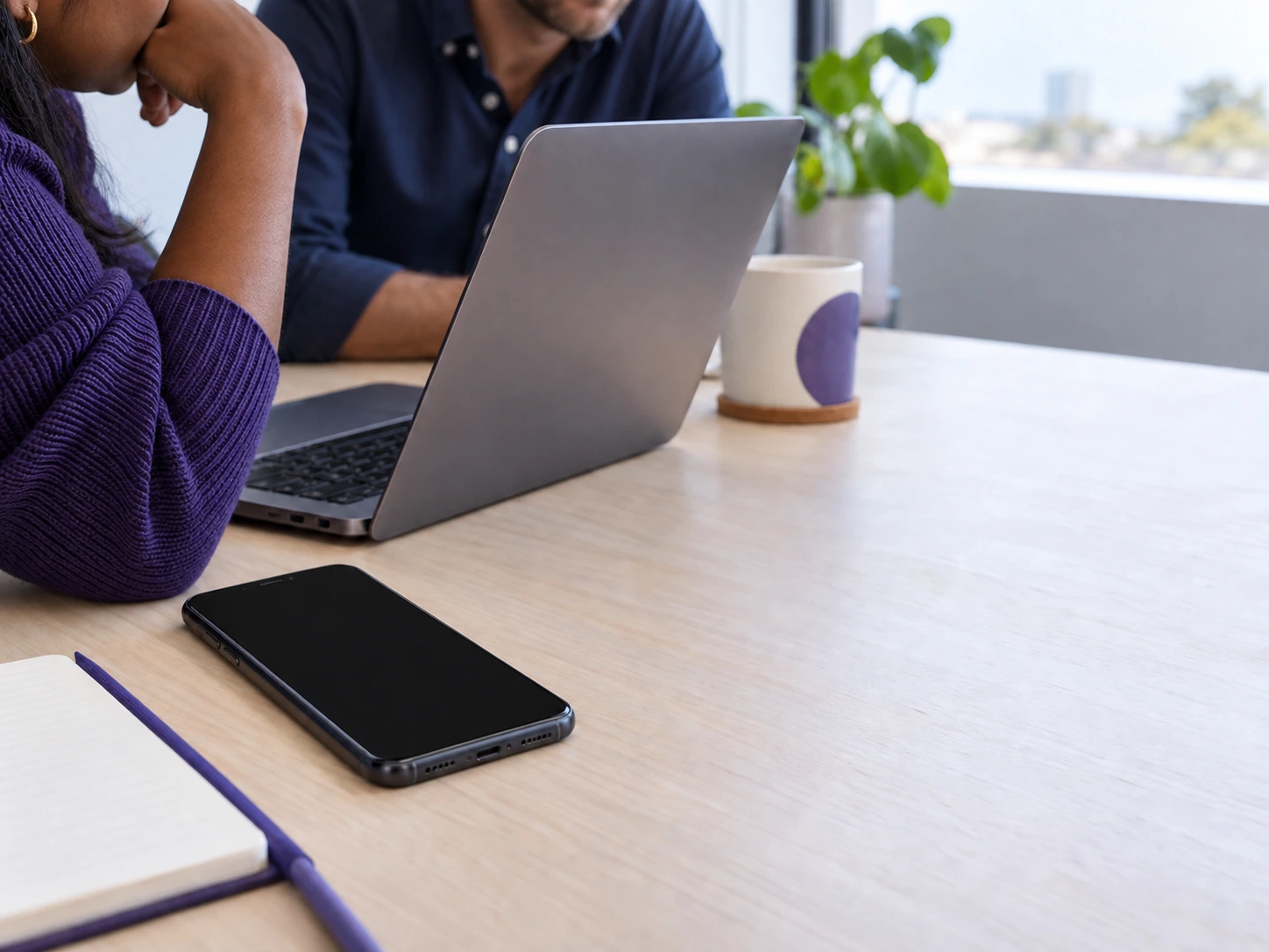 A phone on a pale desk beside a notebook, its screen dark